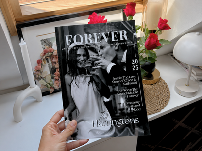 A hand holds a copy of Forever magazine featuring a black-and-white wedding photo of The Harringtons, set against a decorated home interior with red roses and a white table.